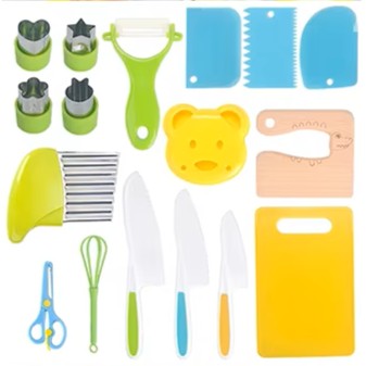 A collection of children's kitchen utensils including colorful cutting boards, knives, scissors, a whisk, peeler, and other cooking tools laid out on a white surface.