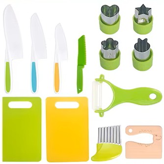 A collection of children's kitchen utensils including colorful cutting boards, knives, scissors, a whisk, peeler, and other cooking tools laid out on a white surface.