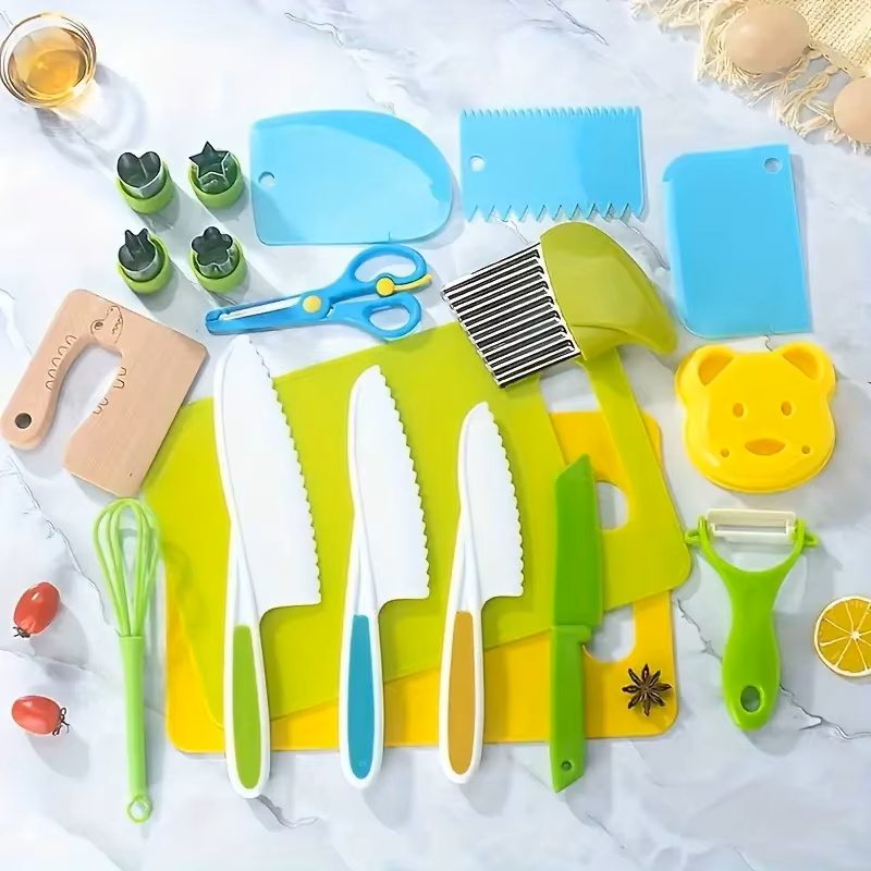 A collection of children's kitchen utensils including colorful cutting boards, knives, scissors, a whisk, peeler, and other cooking tools laid out on a white surface.