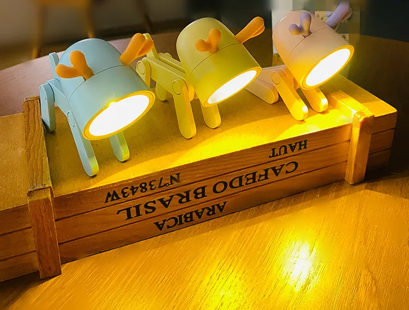 Three cartoon-style lamps on a wooden crate with visible brand name.