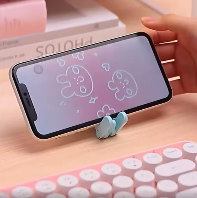 Phone with a cartoon character on screen held by a blue phone stand on a pink surface.