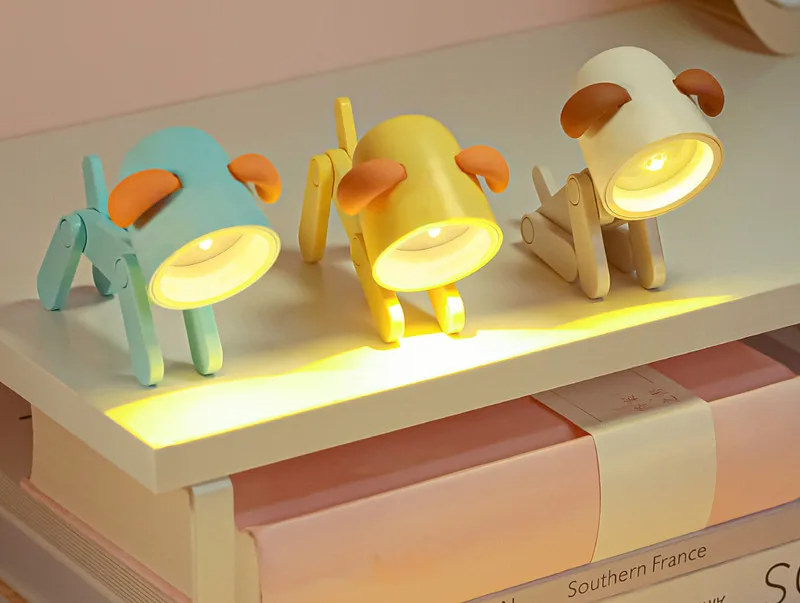 Three cartoon dog-shaped night lights on a shelf with a soft pink background.