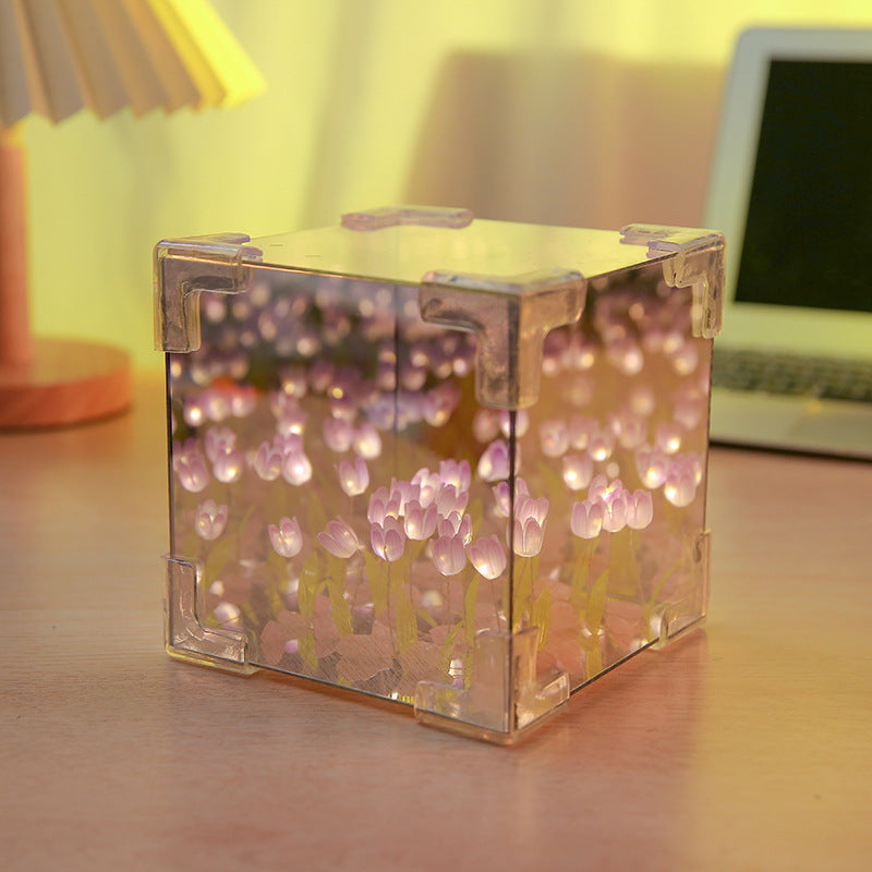 Two LED tulip cubes with multicolored lights, placed on a table surface, likely made of plastic, with a warm light atmosphere in the background.
