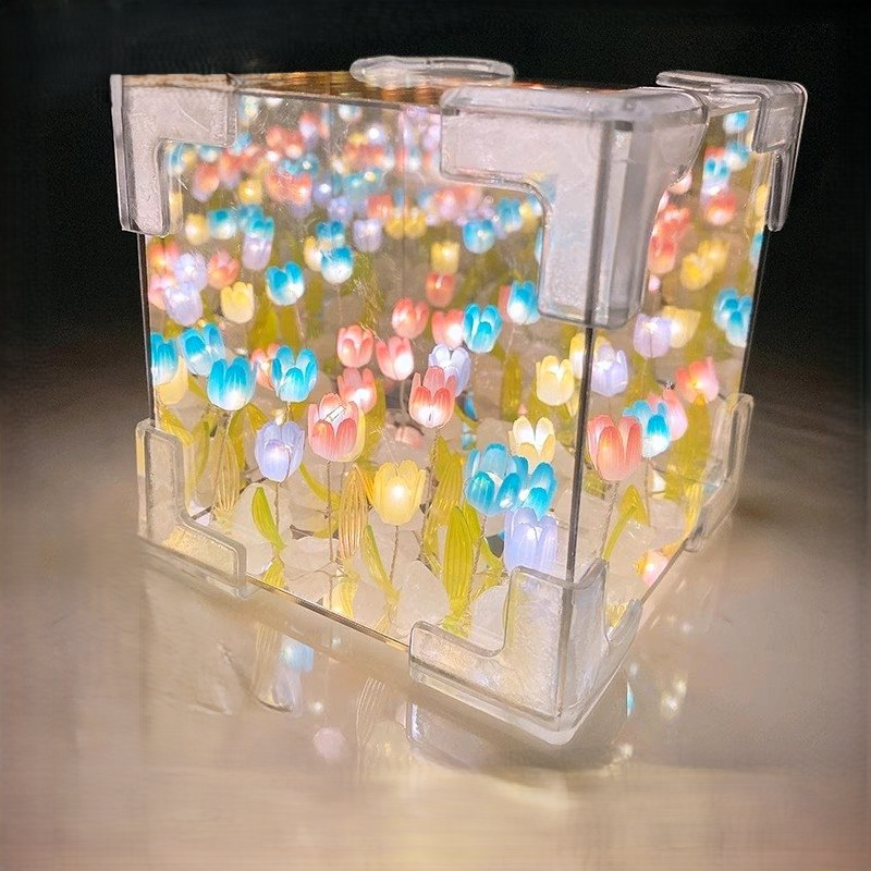 Two LED tulip cubes with multicolored lights, placed on a table surface, likely made of plastic, with a warm light atmosphere in the background.