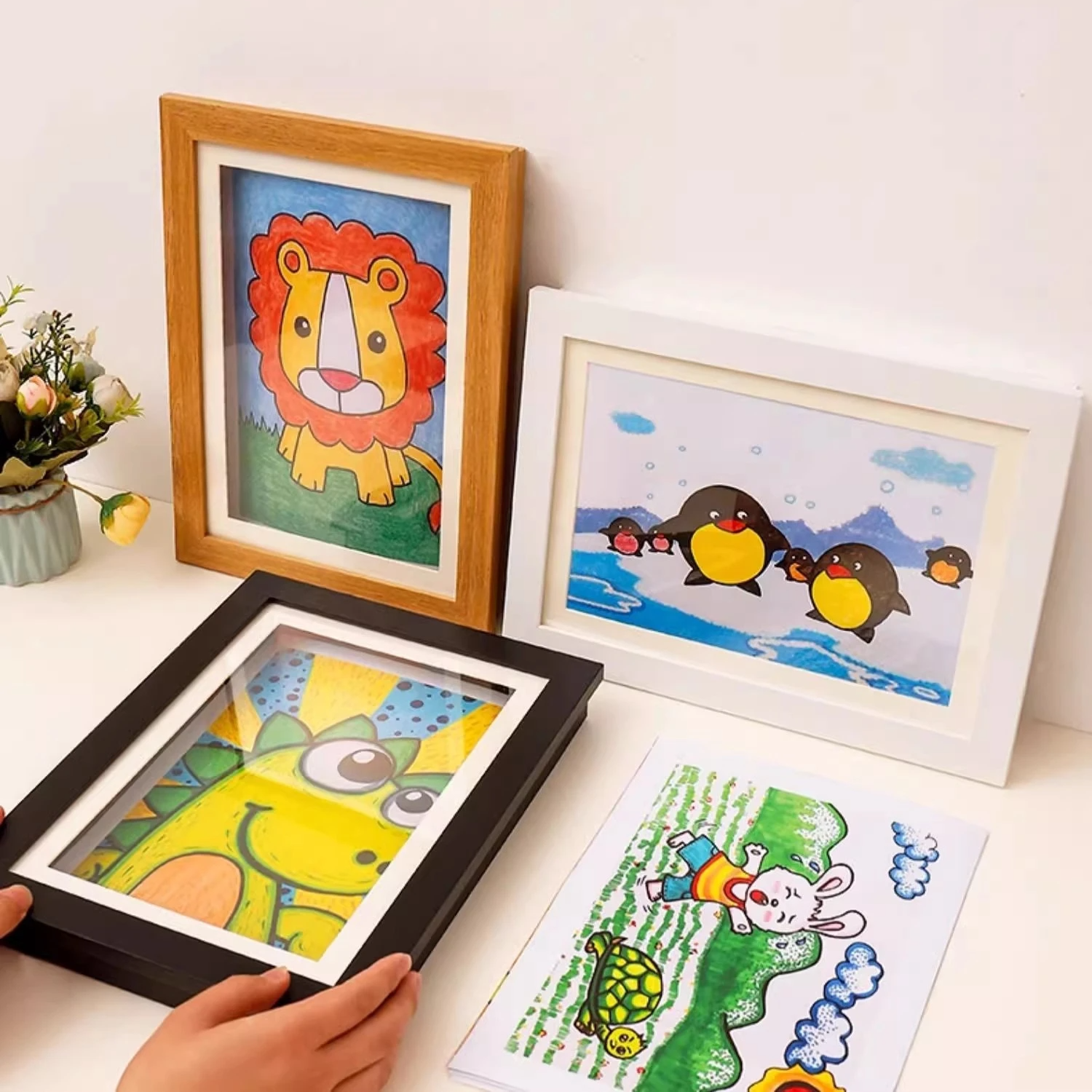 Framed children's artwork of a lion, penguins, and a bear on a table.